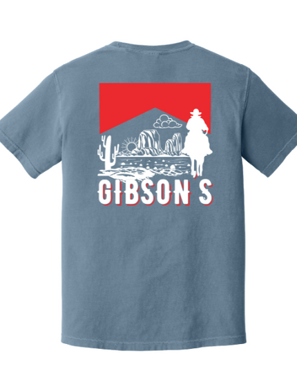 A blue-gray short-sleeve t-shirt shown from the back, featuring a large graphic print with a red rectangle, white western desert illustration, and the word 'GIBSON'S' in white outlined letters.