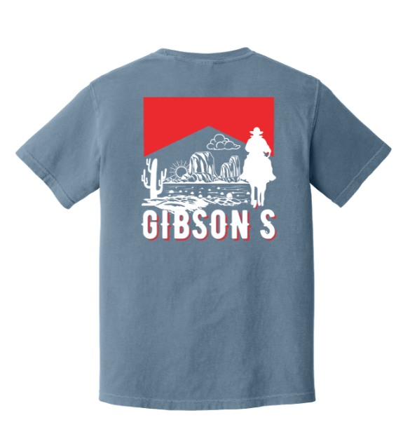 A blue-gray short-sleeve t-shirt shown from the back, featuring a large graphic print with a red rectangle, white western desert illustration, and the word 'GIBSON'S' in white outlined letters.