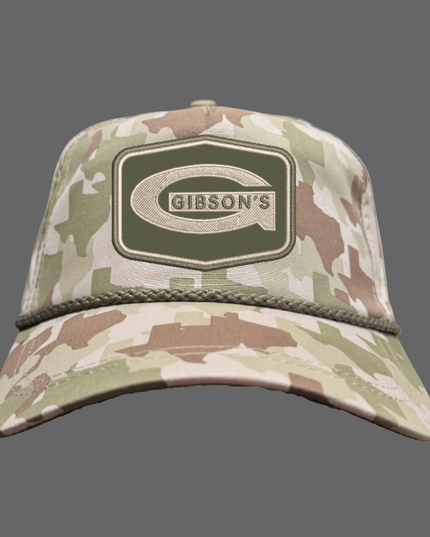 A camouflage baseball cap featuring a prominent Gibson's logo patch on the front, set against a plain white background.